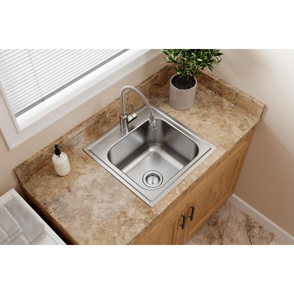 Stainless steel drop-in laundry sink with single bowl installed in wood vanity with granite countertop.