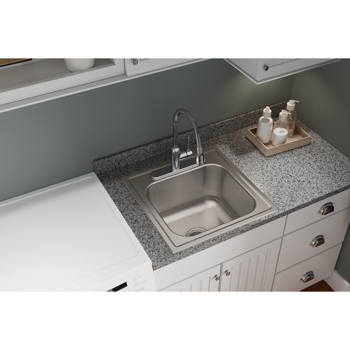 Stainless steel drop-in laundry sink with single bowl and faucet installed in granite countertop with white cabinetry below.