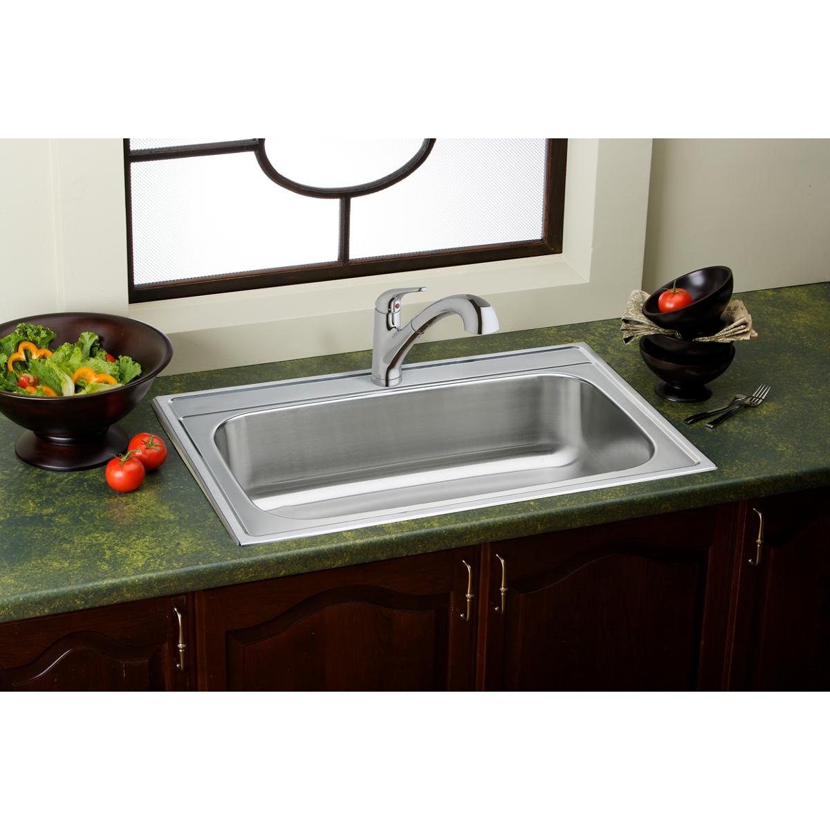 Chrome single-hole kitchen faucet with pull-out spray and lever handle mounted above stainless steel sink on green countertop