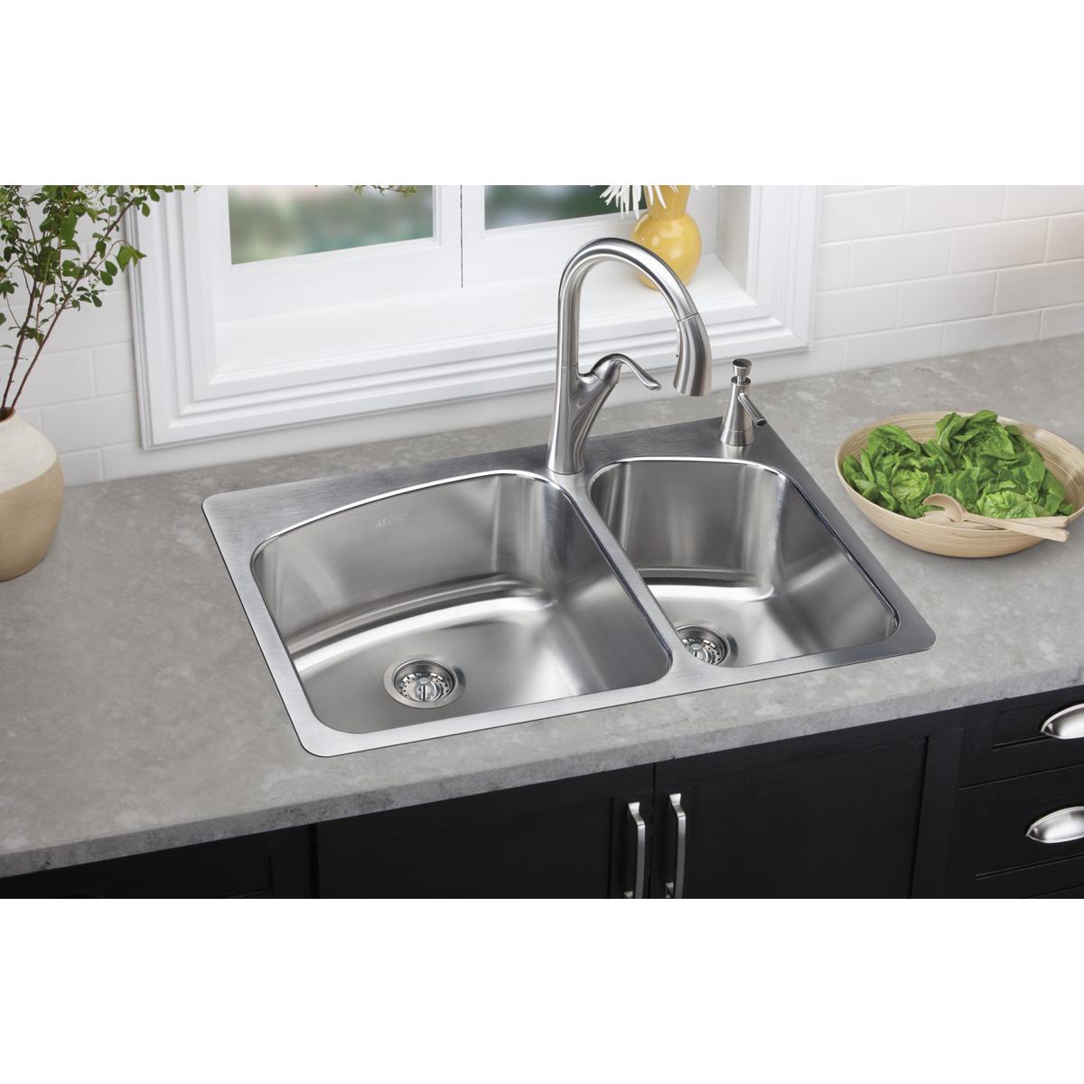 Stainless steel double bowl sink with two drain holes installed in gray countertop with faucet.