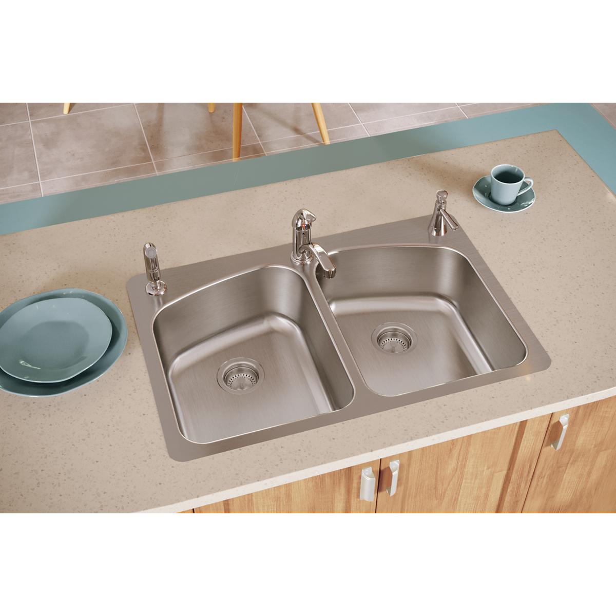 Stainless steel double bowl sink mounted in countertop with two faucets and drain holes.