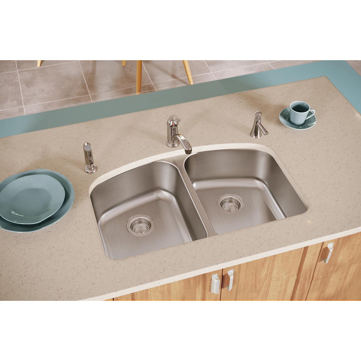 Stainless steel double bowl sink with two faucets and strainers mounted in beige countertop.