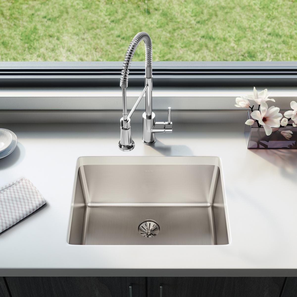 Stainless steel single bowl drop-in sink with four faucet holes and spring-style chrome faucet installed on white countertop.