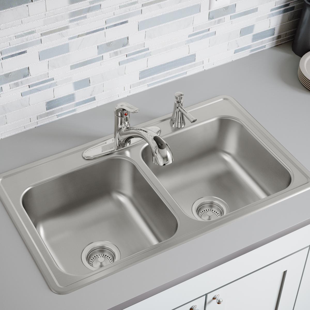 Stainless steel double bowl drop-in sink with two faucets and drain strainers, installed in white countertop.