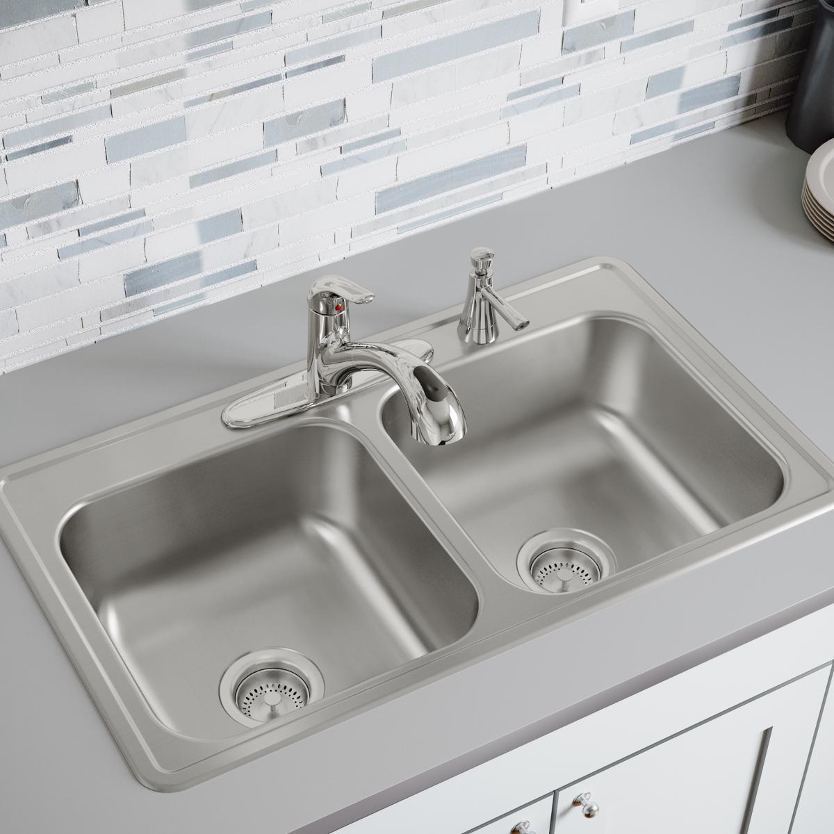 Stainless steel drop-in sink with two equal bowls, three faucet holes, and drain strainers installed in white countertop.