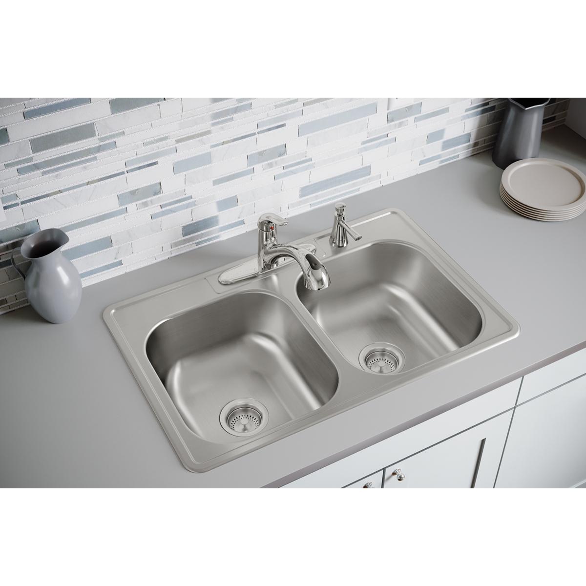 Stainless steel double bowl drop-in sink with four faucet holes, chrome faucet, and strainer drains installed in white counte