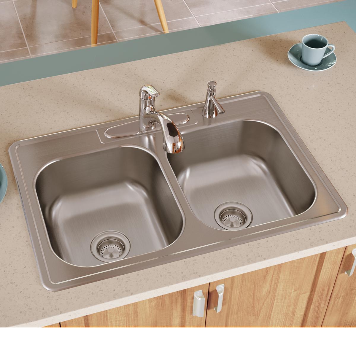 Stainless steel double bowl drop-in sink with two faucets and strainers installed in beige countertop.