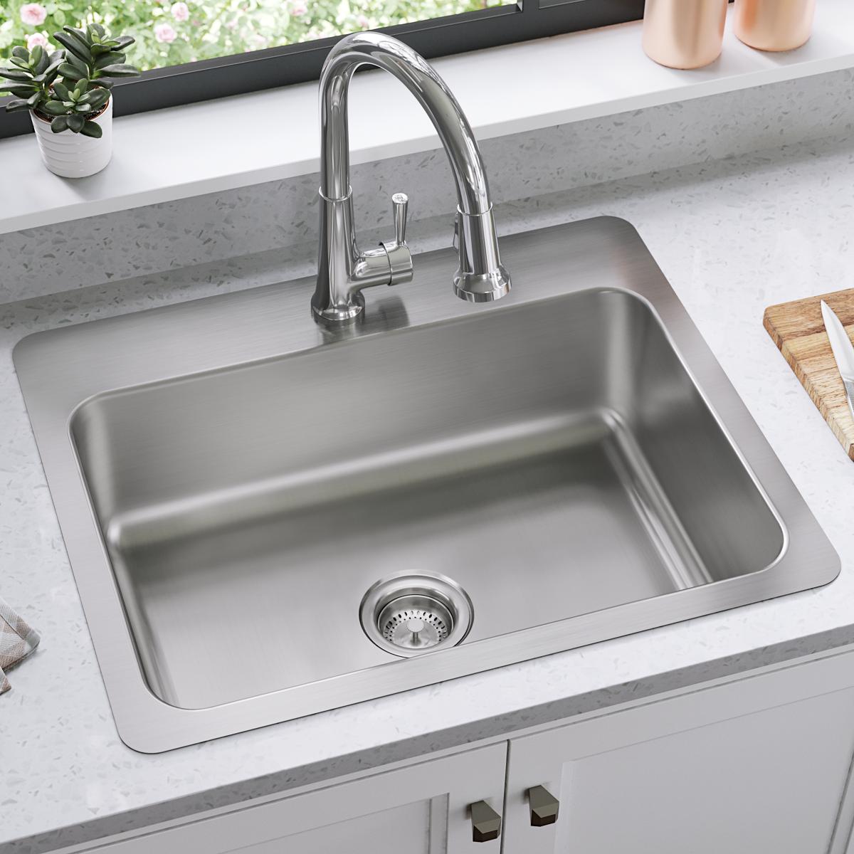 Stainless steel single bowl sink with chrome pull-down faucet and drain strainer installed in gray countertop.
