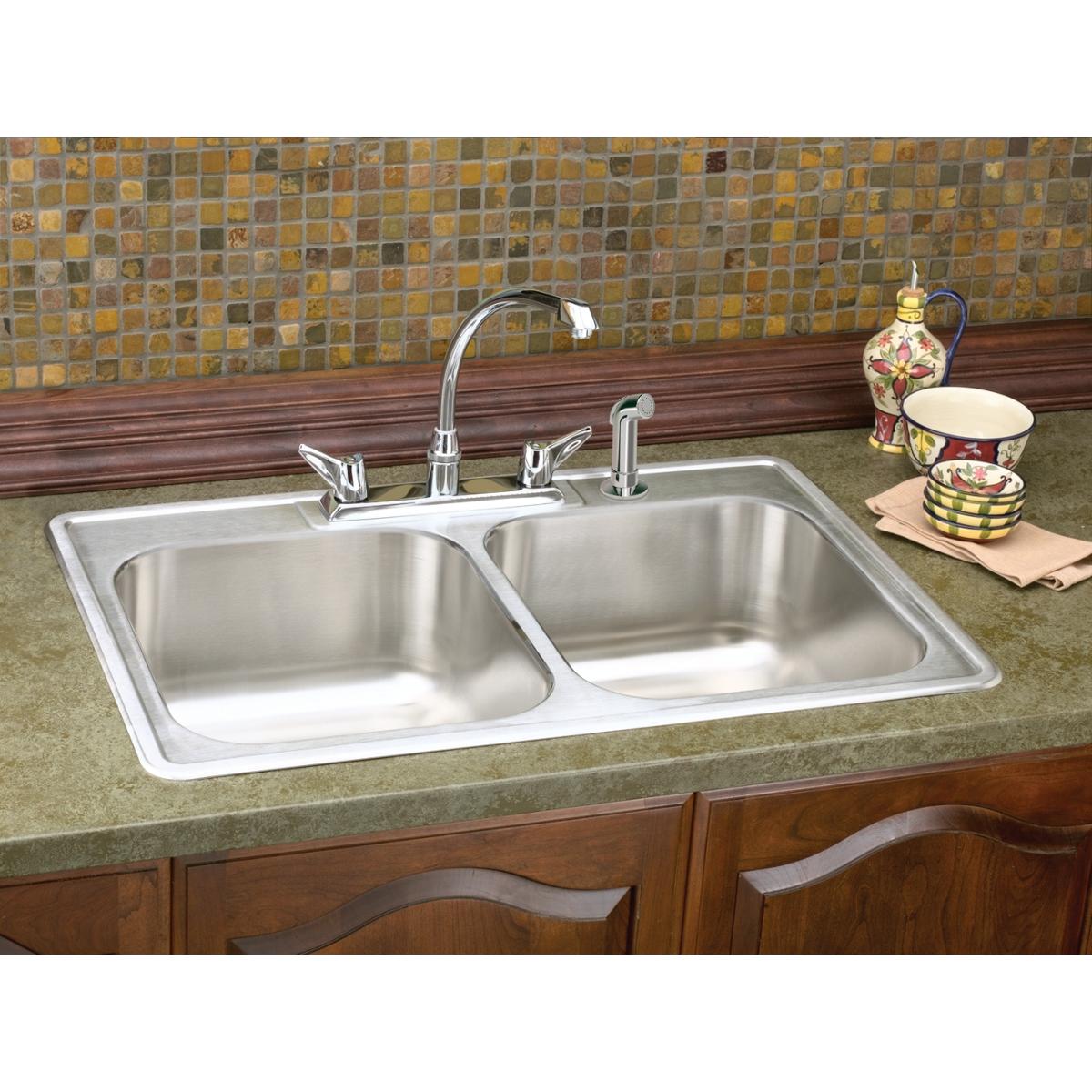 Stainless steel double bowl drop-in sink with chrome faucet and five mounting holes installed in green countertop.