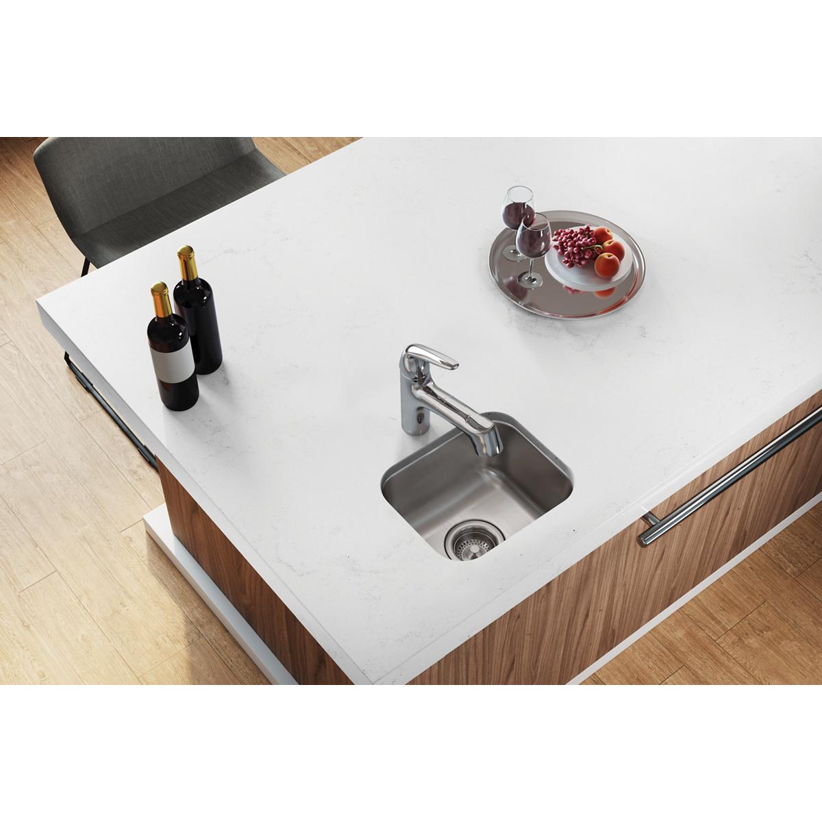 Stainless steel single bowl undermount bar sink installed in white countertop with chrome faucet.