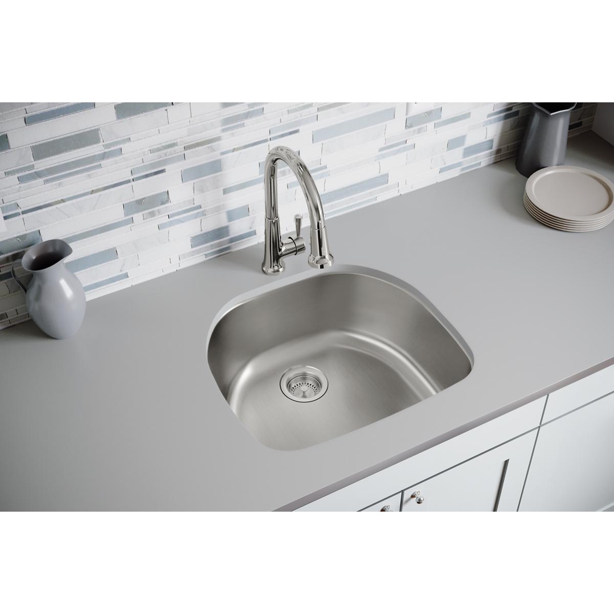 Stainless steel single bowl undermount sink installed in white countertop with chrome faucet and drain strainer visible.