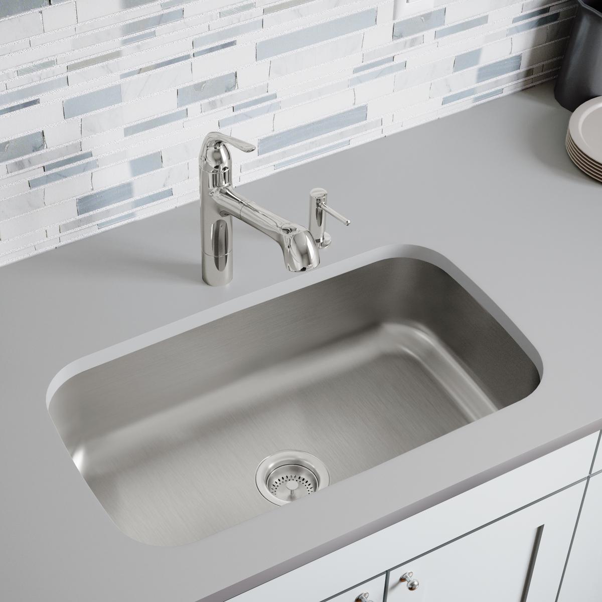Stainless steel undermount sink with single rectangular bowl and drain strainer, installed beneath white countertop with chro