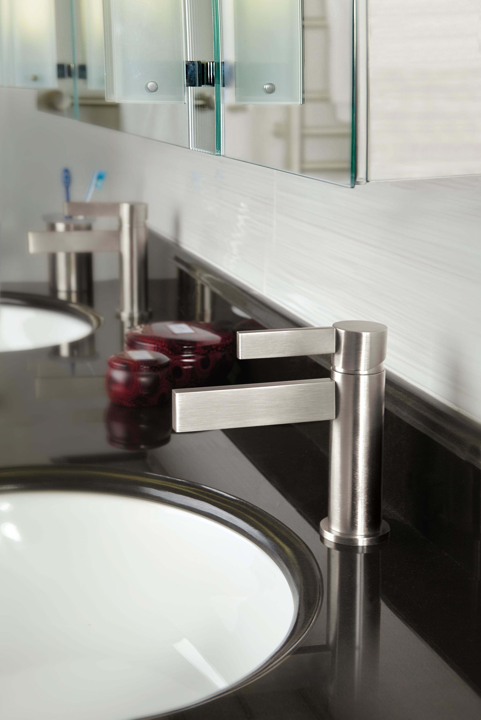 Polished chrome single-hole lavatory faucet with rectangular lever handle mounted on black countertop next to white sink.