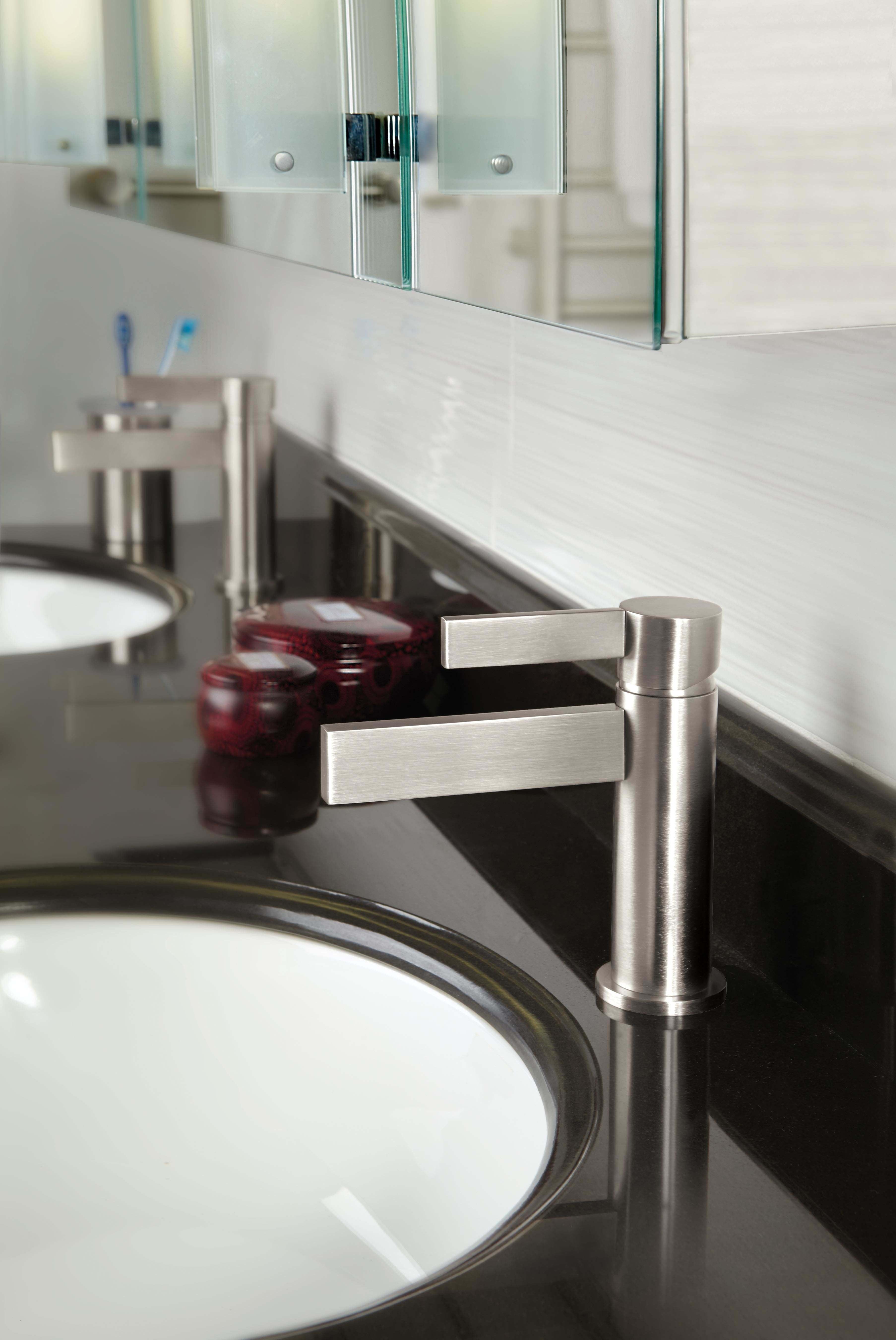 Polished chrome single-hole lavatory faucet with rectangular lever handle mounted on black countertop next to white sink.