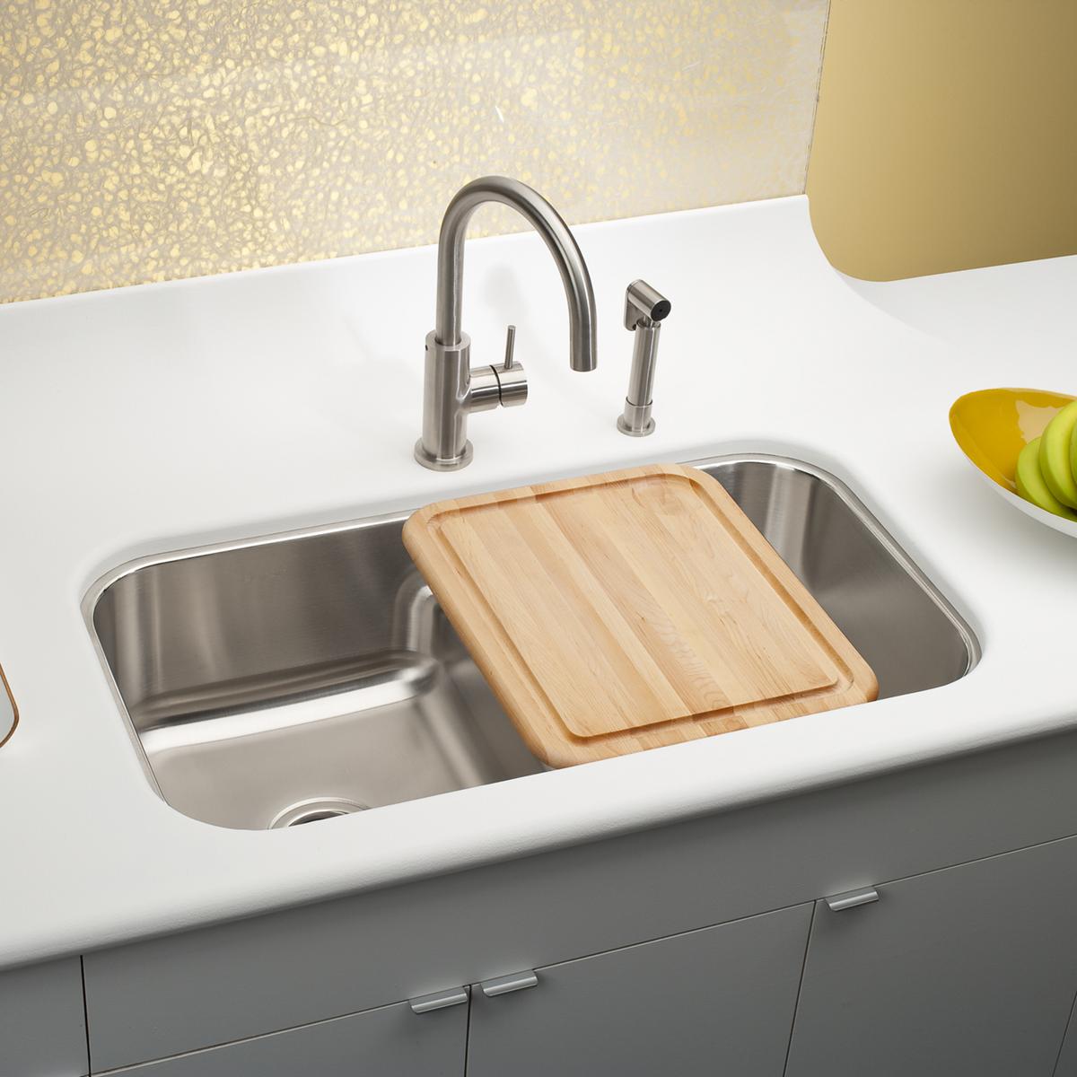 Stainless steel double bowl undermount sink with wooden cutting board divider, installed in white countertop with faucet.