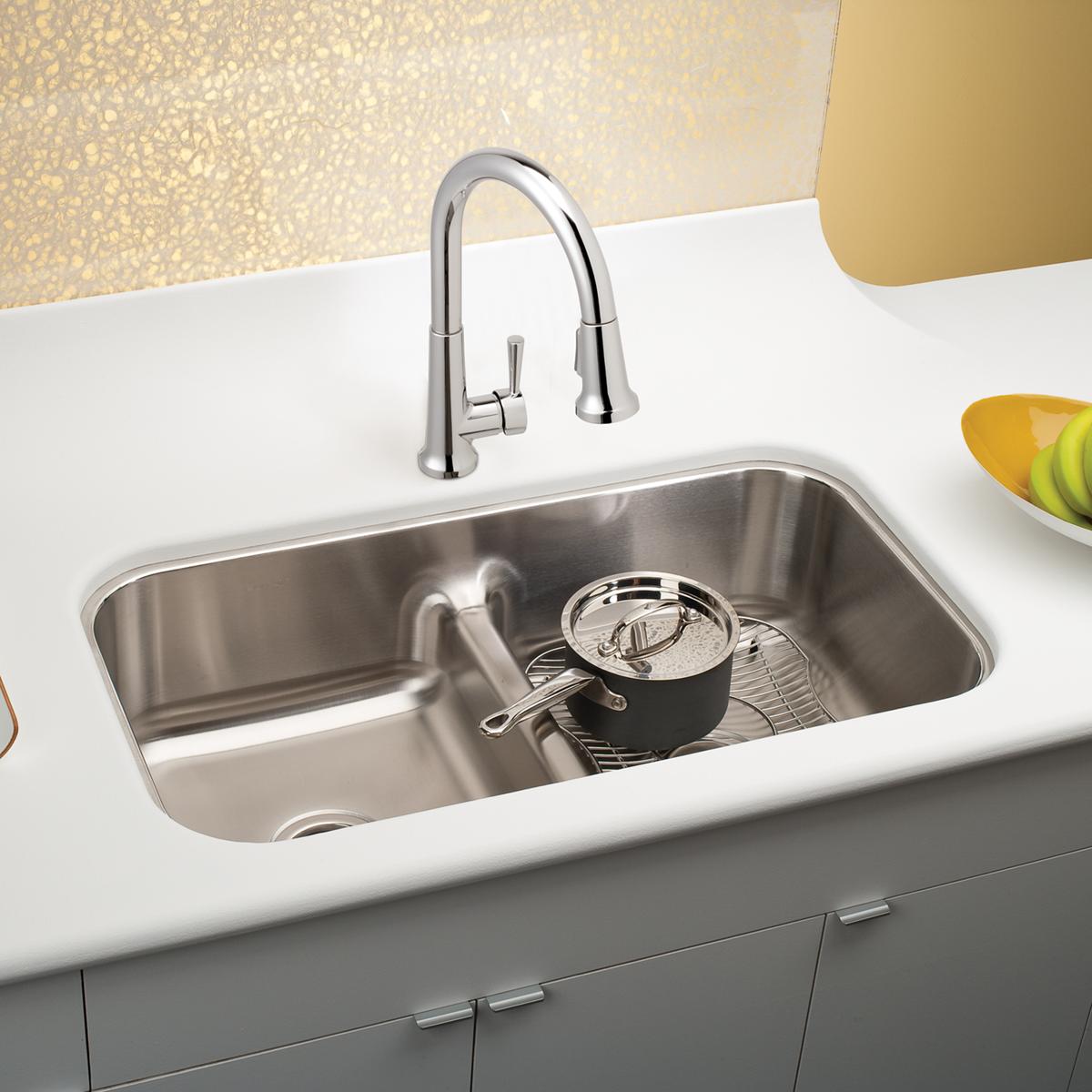 Stainless steel double bowl undermount sink with divider and chrome pull-down faucet installed in white countertop.