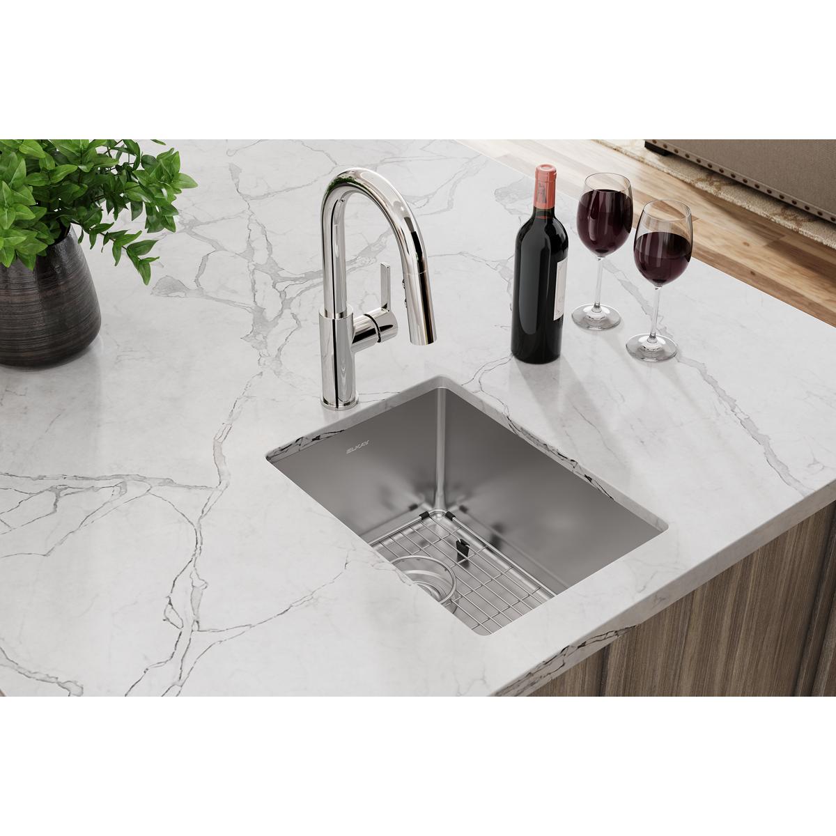 Stainless steel undermount bar sink with chrome faucet, bottom grid, and drain installed in white marble countertop.