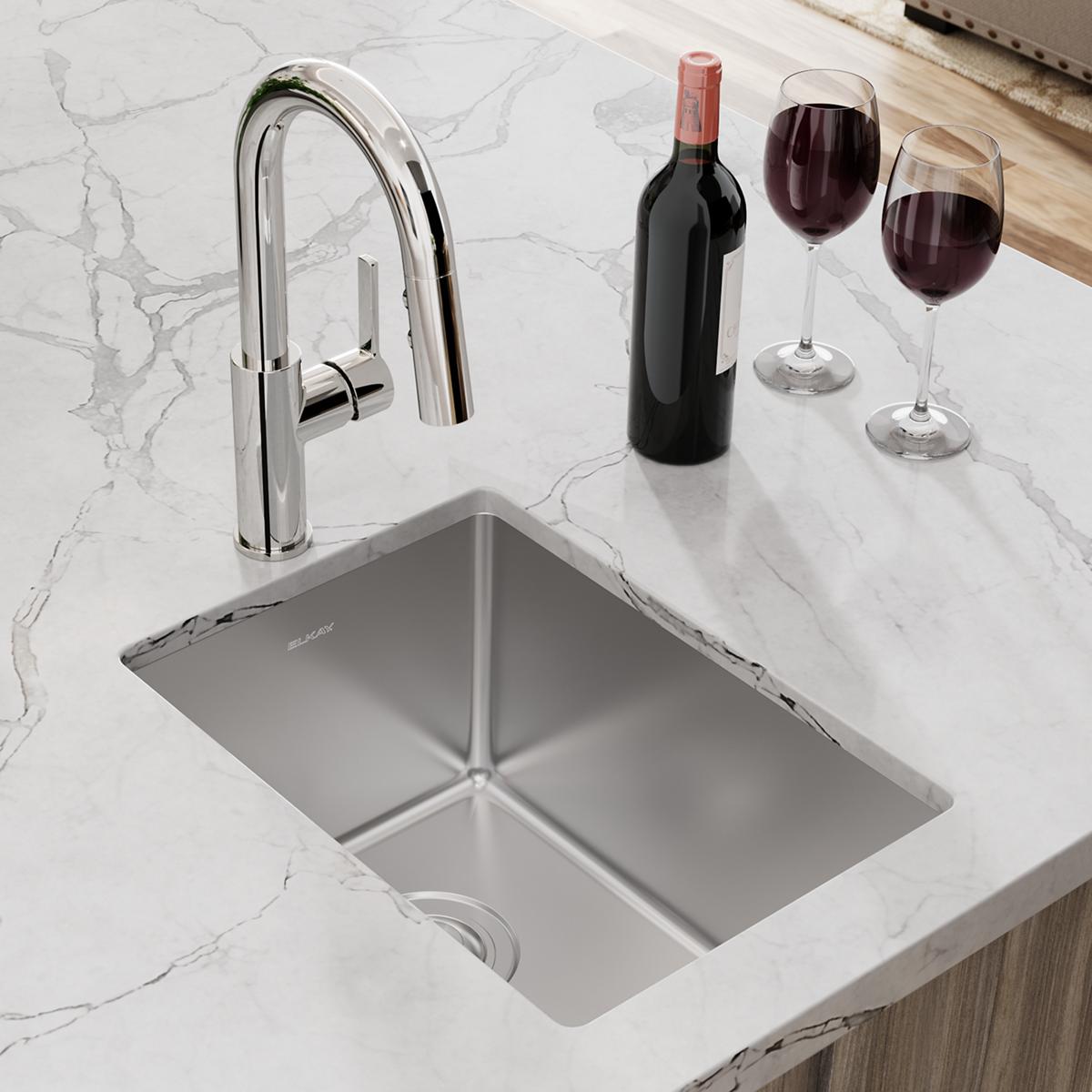 Stainless steel undermount bar sink with chrome pull-down faucet installed in marble countertop, wine bottle and glasses besi