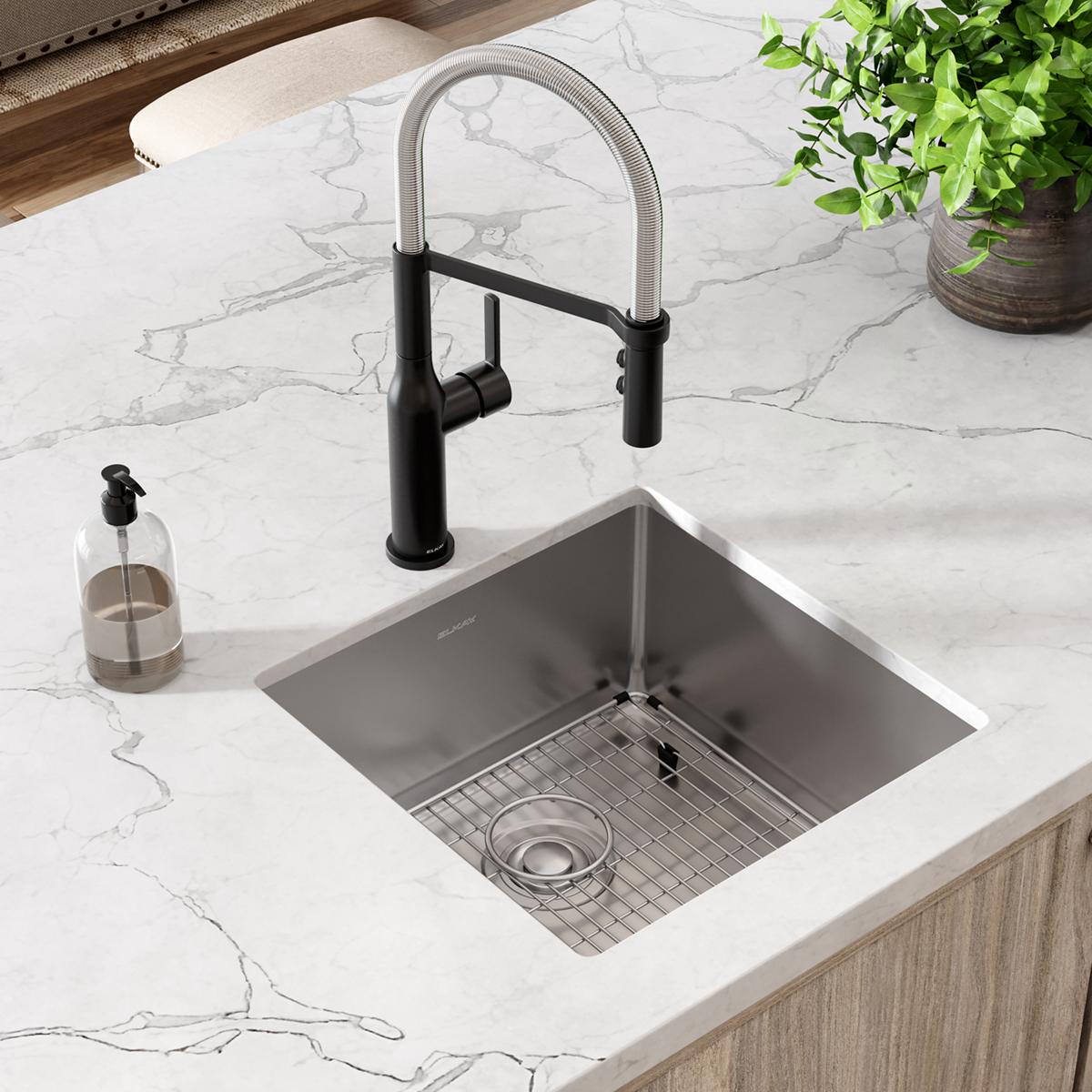 Stainless steel single bowl undermount sink with black pull-down faucet installed in marble countertop, includes grid and dra