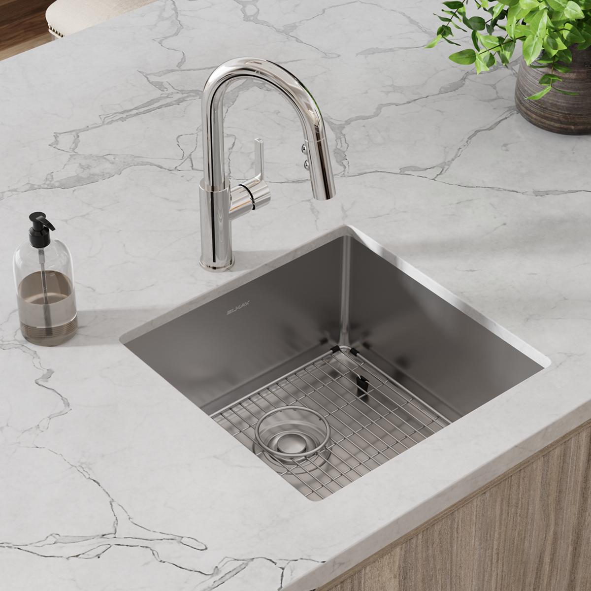 Stainless steel undermount sink with grid and drain installed in marble countertop, paired with chrome pull-down faucet.