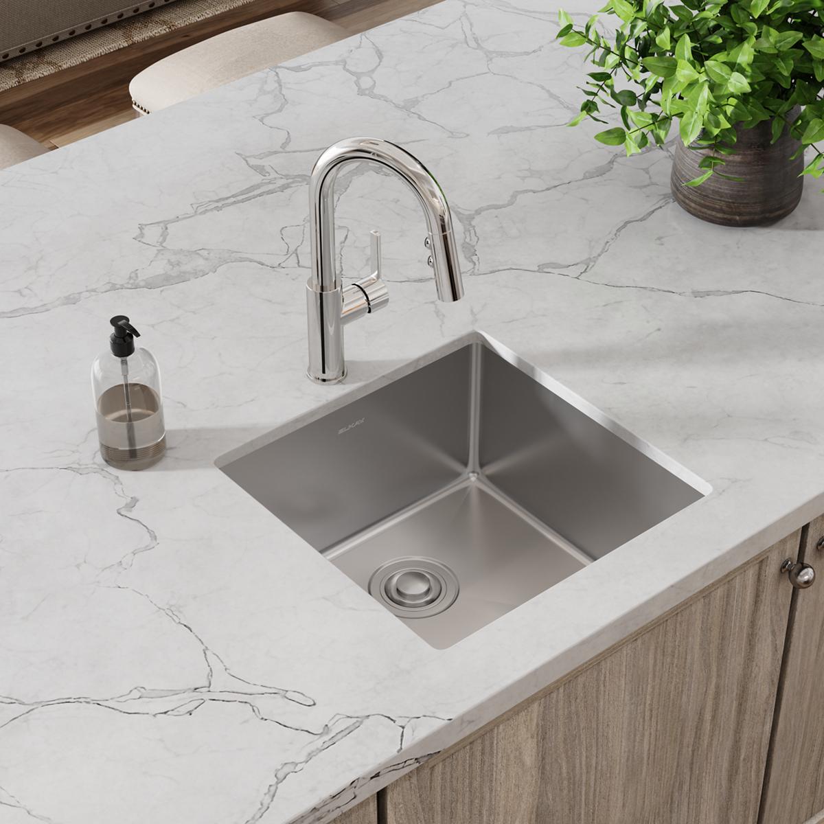 Stainless steel single bowl undermount sink with chrome pull-down faucet installed in white marble countertop.