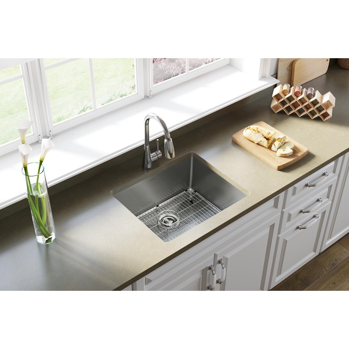 Stainless steel undermount sink installed in white kitchen cabinet with faucet, drain grid, and white countertop.
