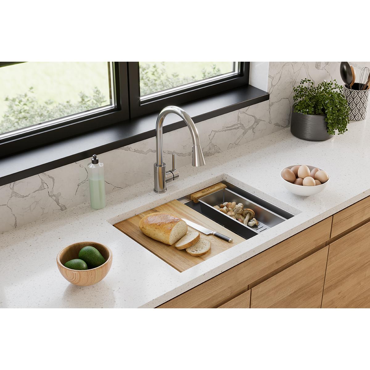 Stainless steel colander with wood handles displayed on a kitchen countertop near a sink.