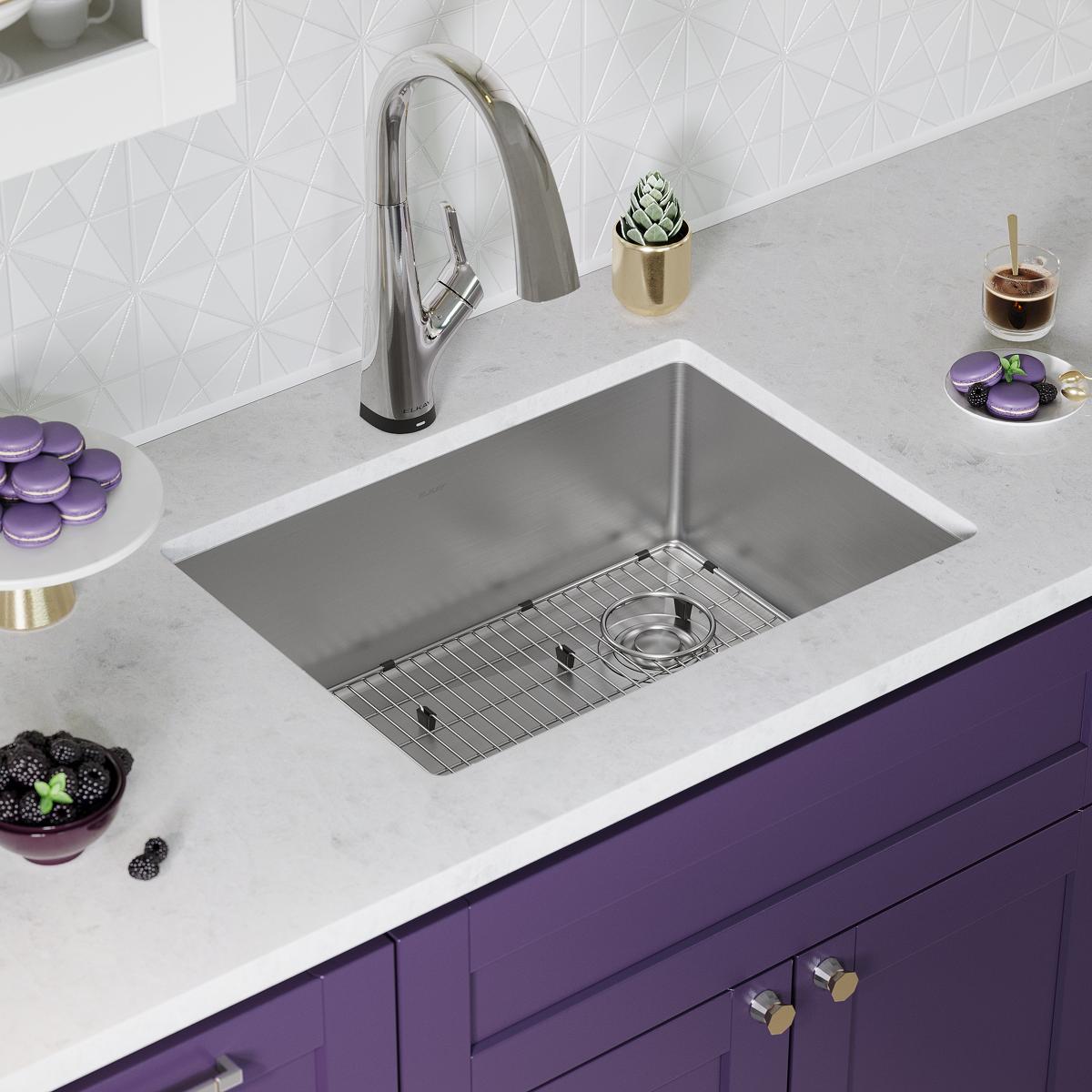 Stainless steel undermount sink bowl with chrome pull-down faucet installed in white countertop above purple cabinetry.