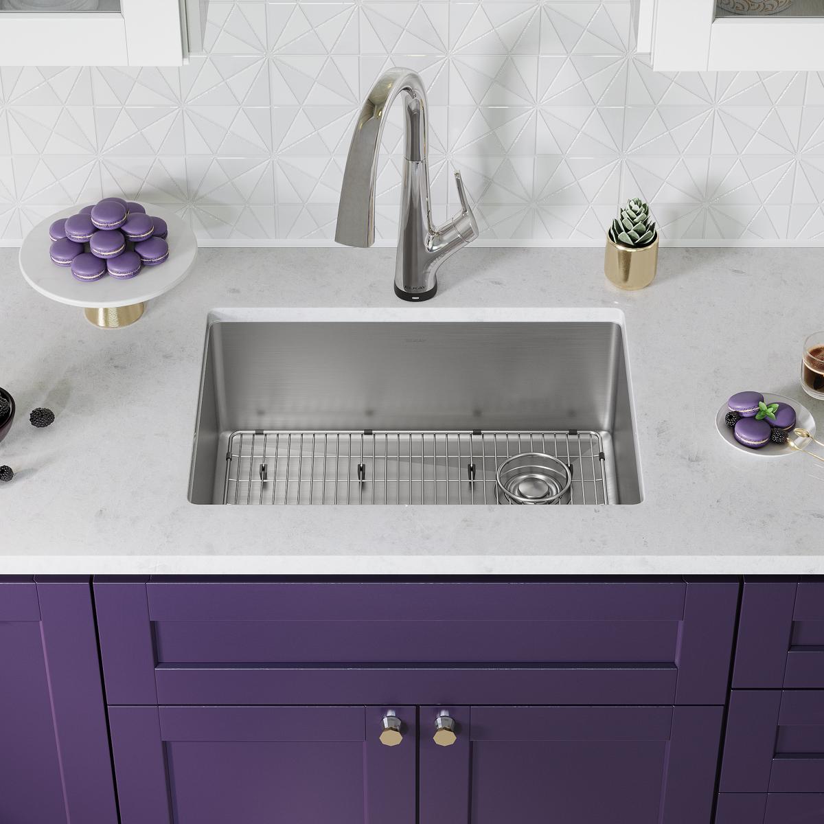 Stainless steel single bowl undermount sink with filtered faucet installed in white countertop above purple cabinetry.