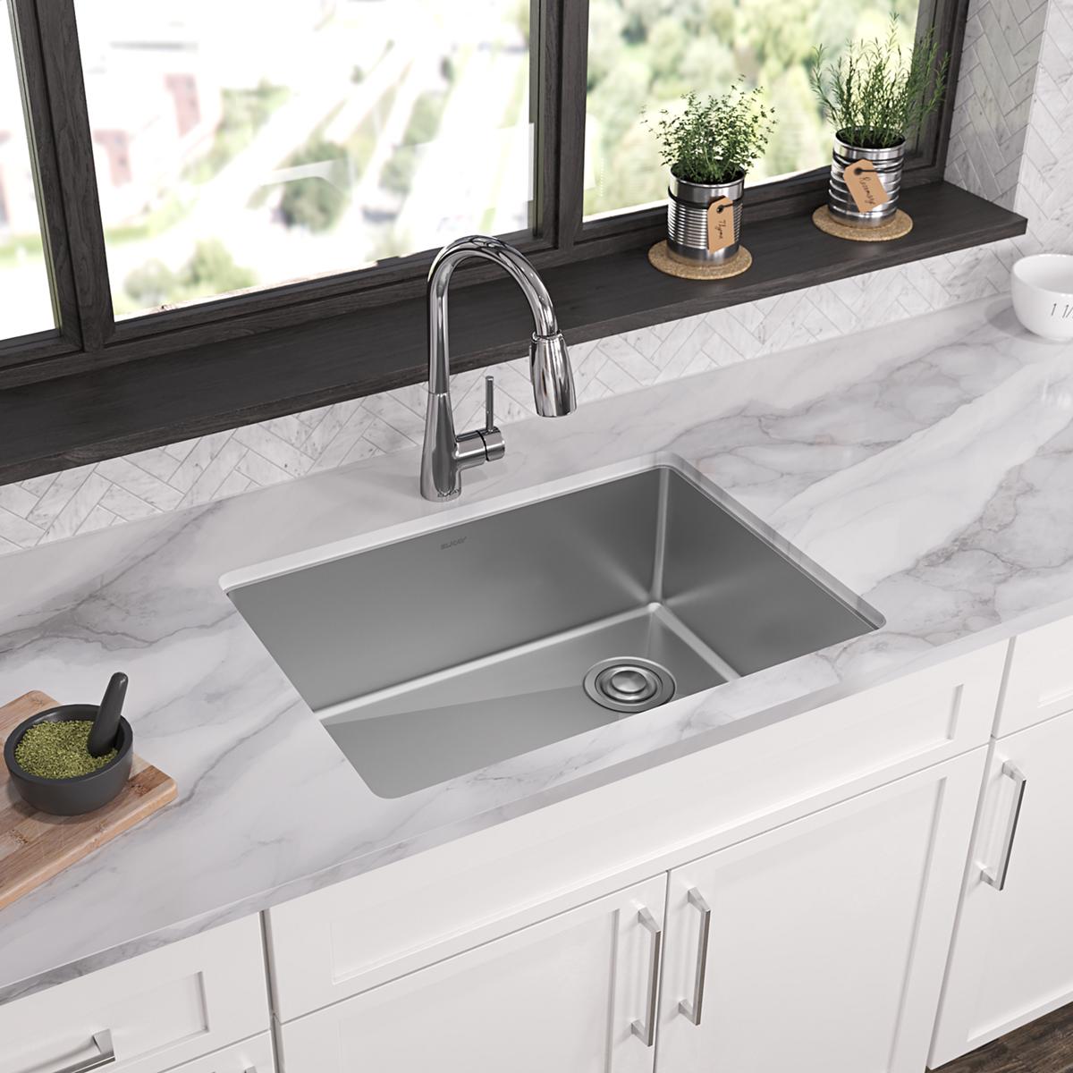 Stainless steel single bowl undermount sink installed in white marble countertop with chrome faucet.