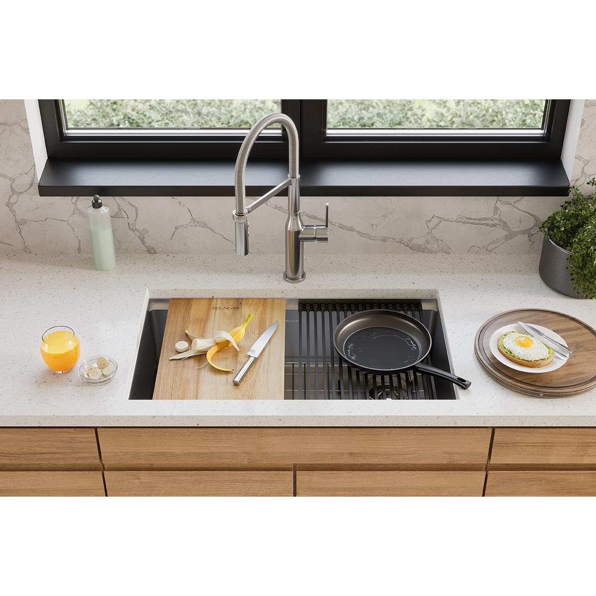 Light brown acacia hardwood cutting board with sliced lemon and knife on kitchen sink counter.