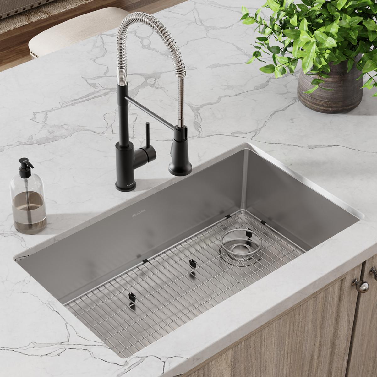 Stainless steel undermount sink with black pull-down faucet, bottom grid, and drain installed in marble countertop.