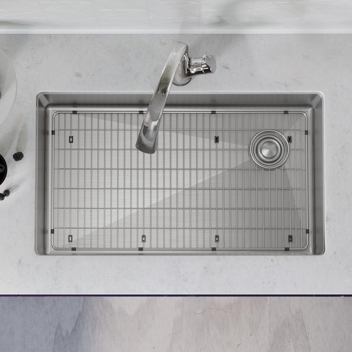 Stainless steel undermount sink with single bowl, grid insert, and chrome filtered faucet mounted on countertop, viewed from 