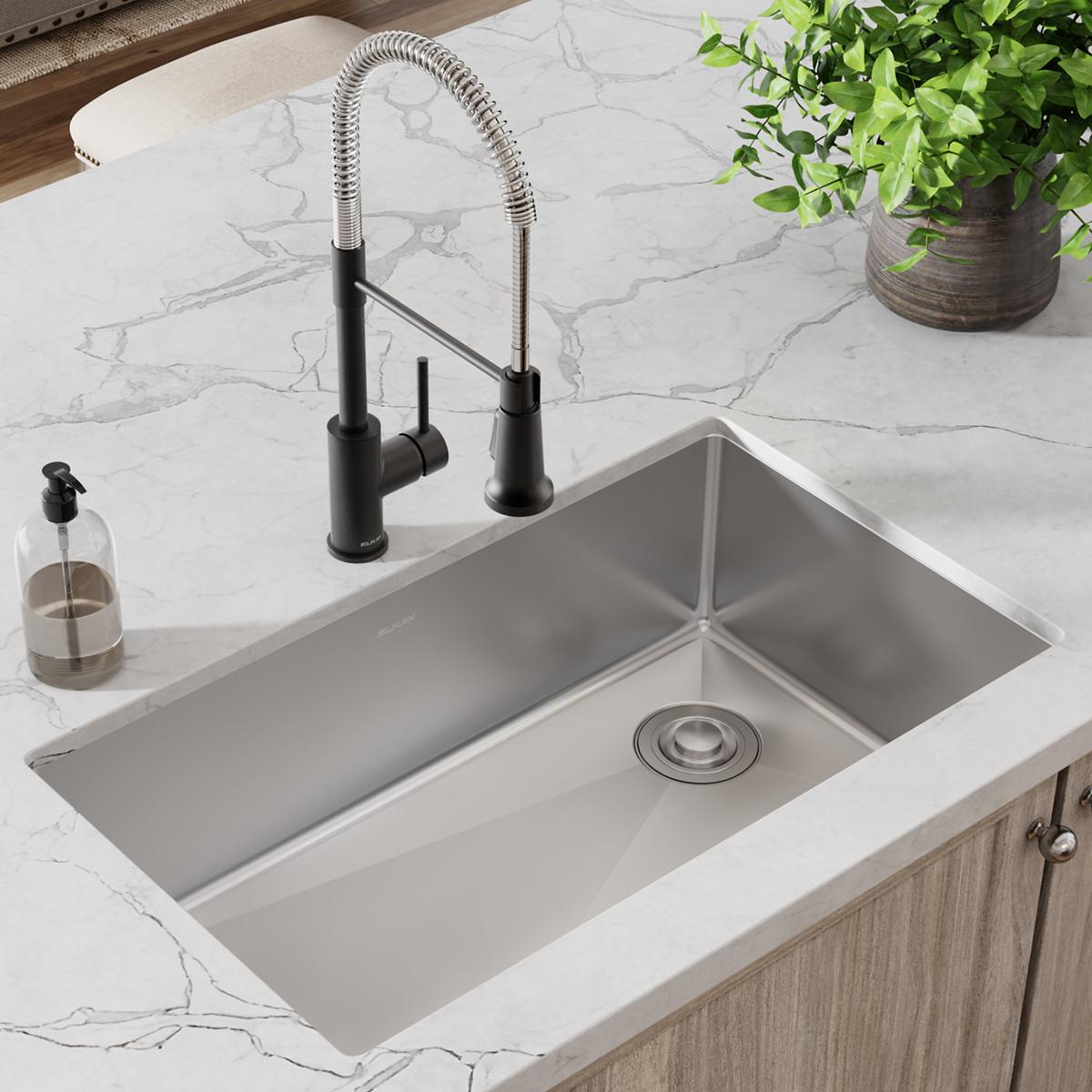 Stainless steel single bowl undermount sink with black pull-down faucet installed in white marble countertop.