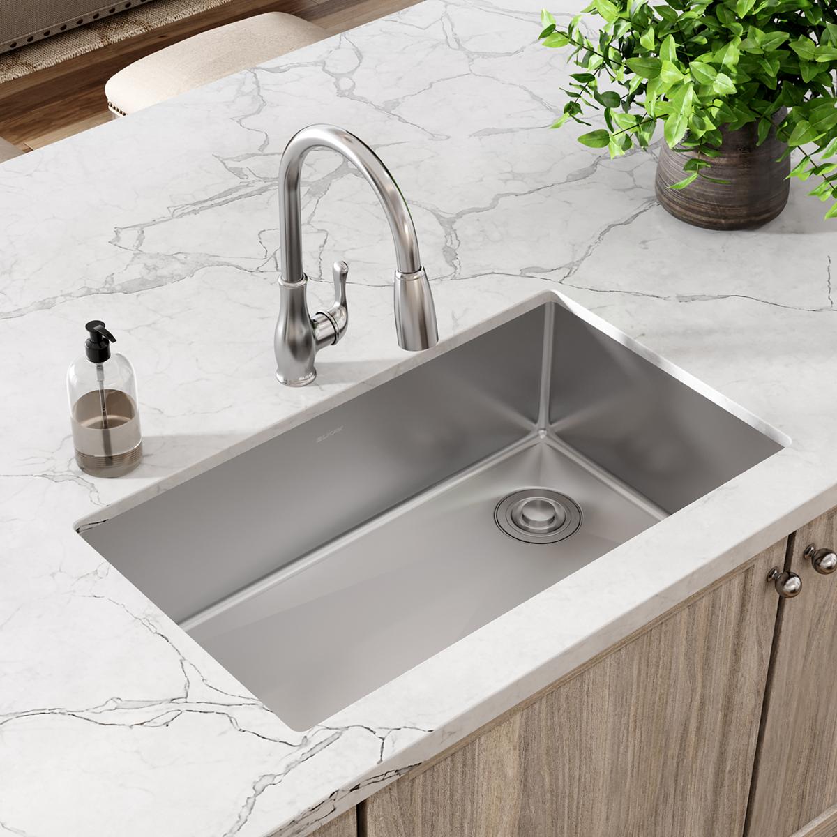 Stainless steel undermount kitchen sink with single bowl installed in white marble countertop, paired with chrome pull-down f