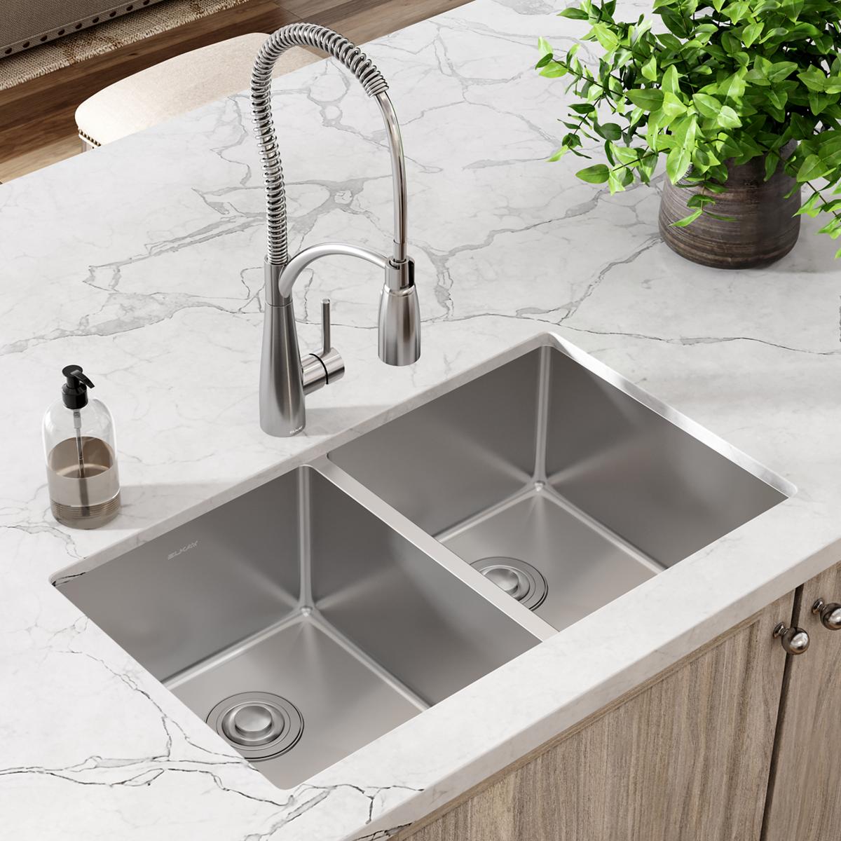 Stainless steel double bowl undermount sink installed in white marble countertop with pull-down faucet.