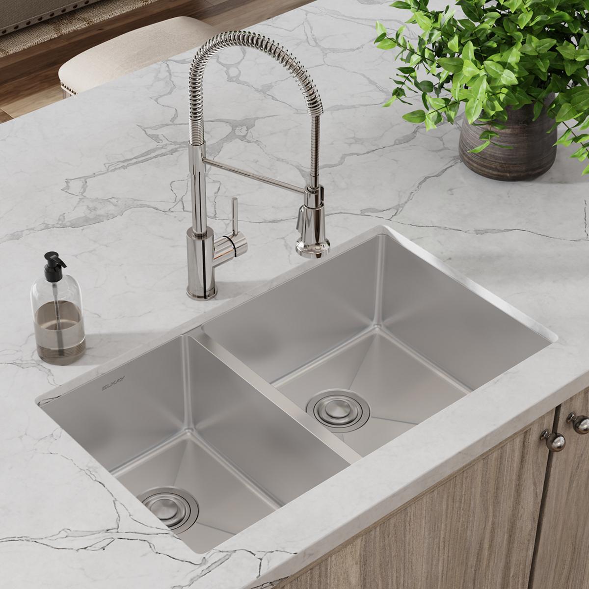 Stainless steel double bowl undermount sink with chrome pull-down faucet and drain installed in marble countertop.
