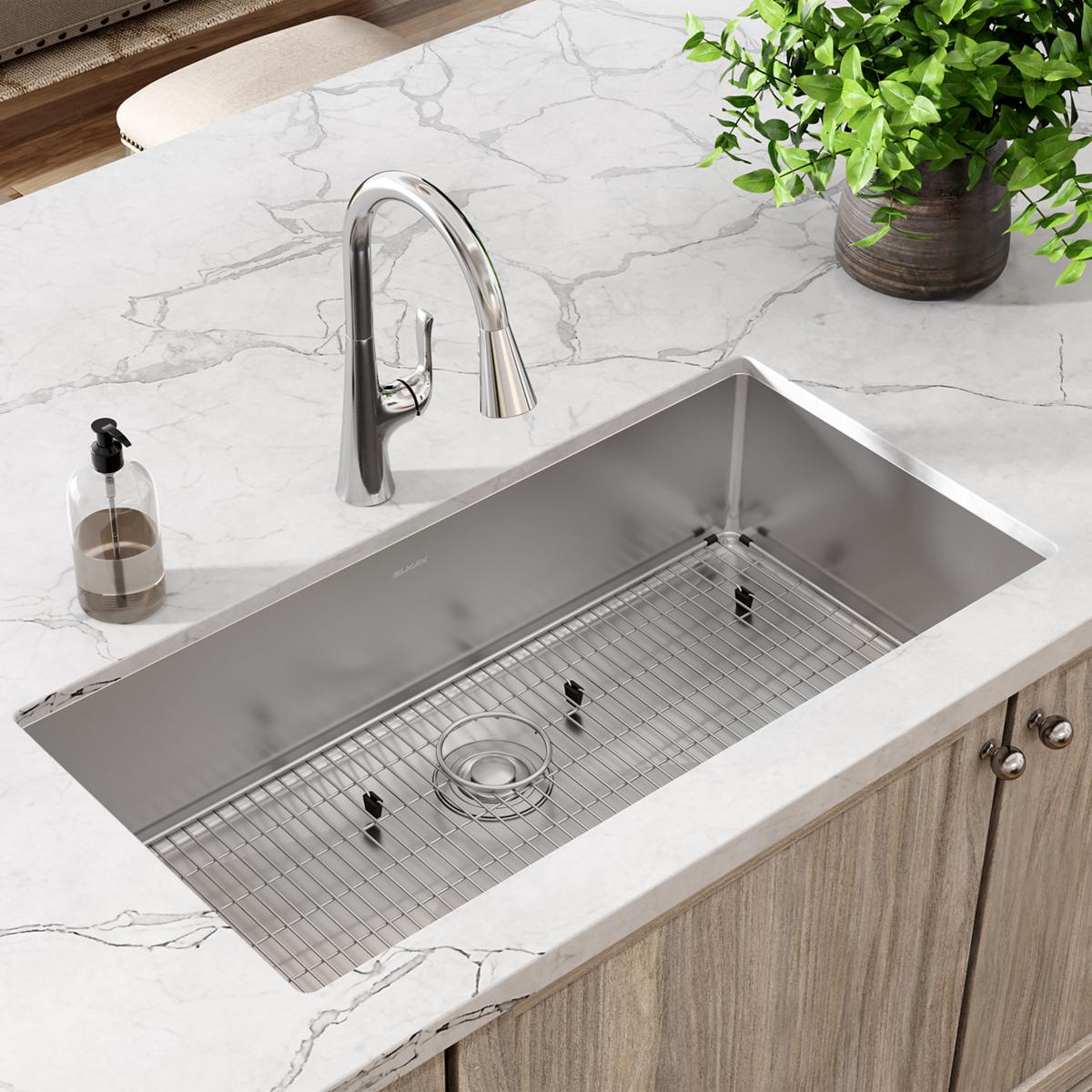 Stainless steel rectangular undermount sink with single bowl, grid rack, and chrome pull-down faucet installed in marble coun