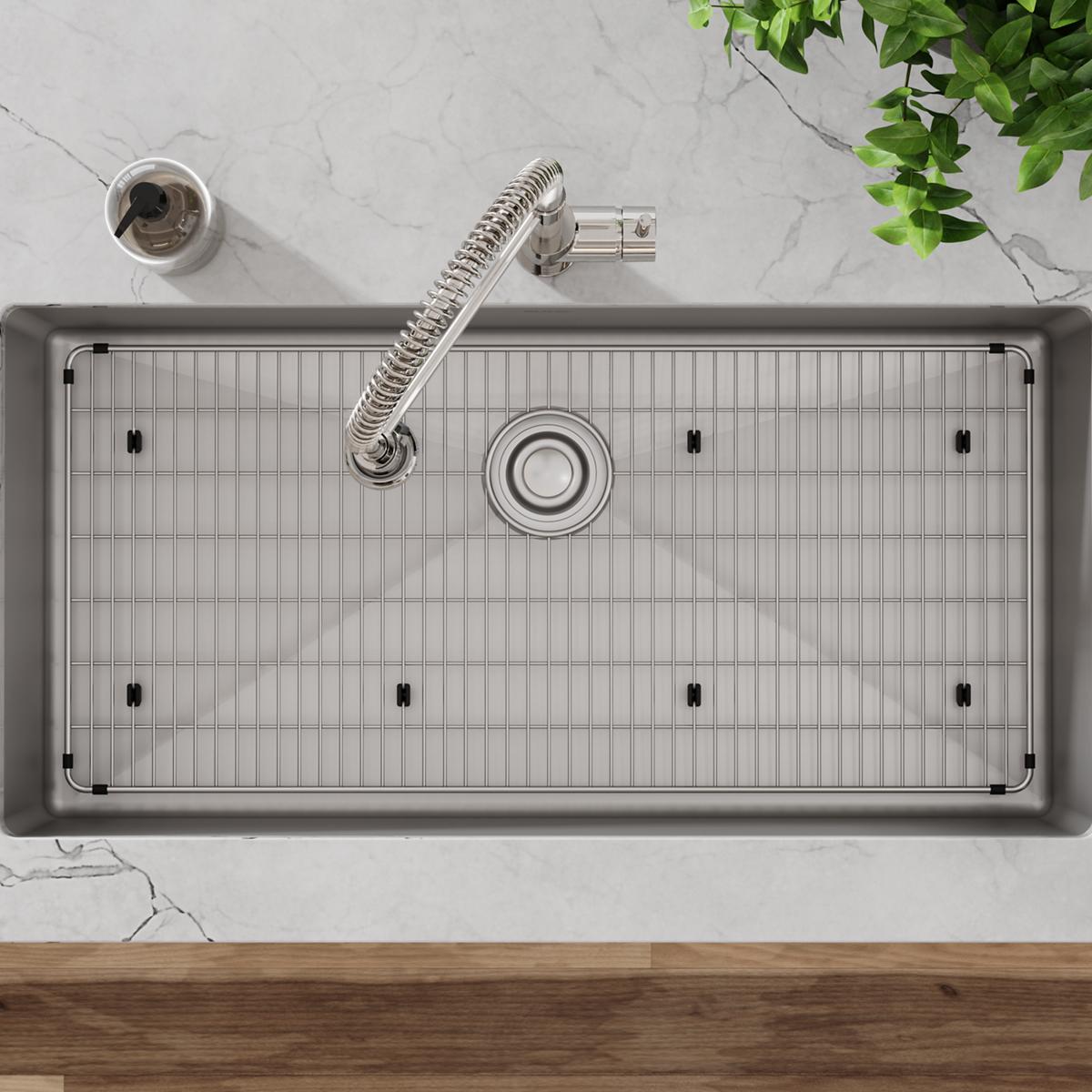 Stainless steel sink grid with vertical slat pattern and rubber feet, positioned in undermount sink basin.
