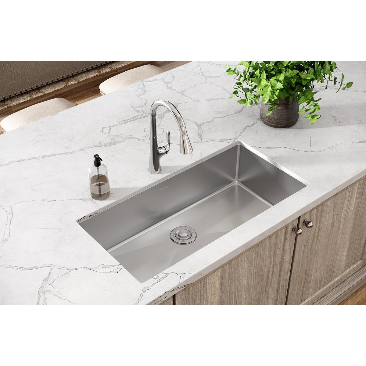 Stainless steel undermount sink installed in white marble countertop with chrome faucet and drain visible.