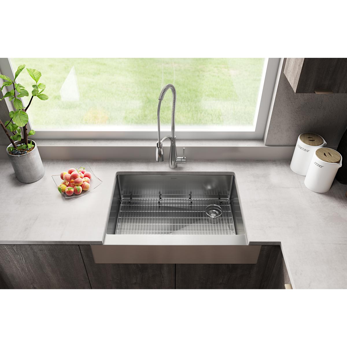 Stainless steel single bowl farmhouse sink with grid insert and spiral pull-down faucet installed in countertop.