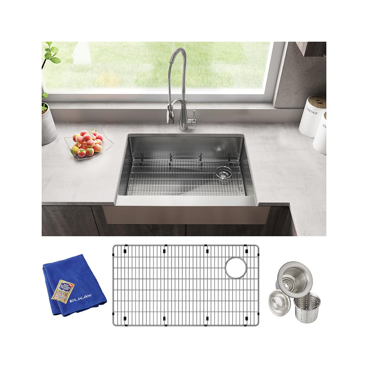 Stainless steel farmhouse sink with spring faucet, grid insert, blue towel, and strainer accessories shown in kitchen window 