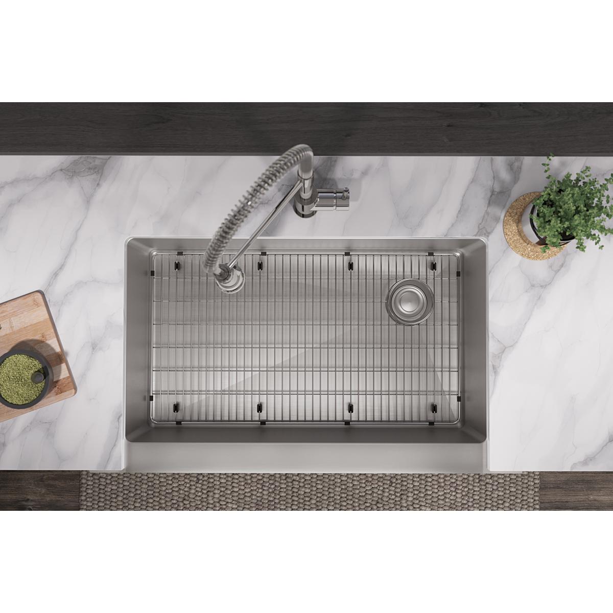 Stainless steel sink grid with parallel slats and mounting feet, shown installed in kitchen sink basin.