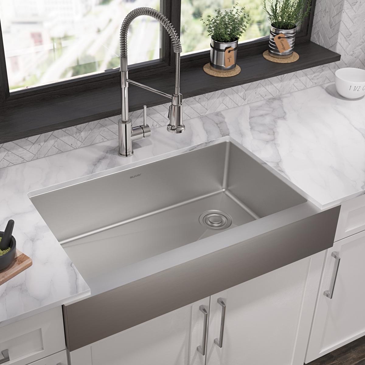 Stainless steel farmhouse sink with single bowl and chrome pull-down faucet installed in marble countertop with white cabinet