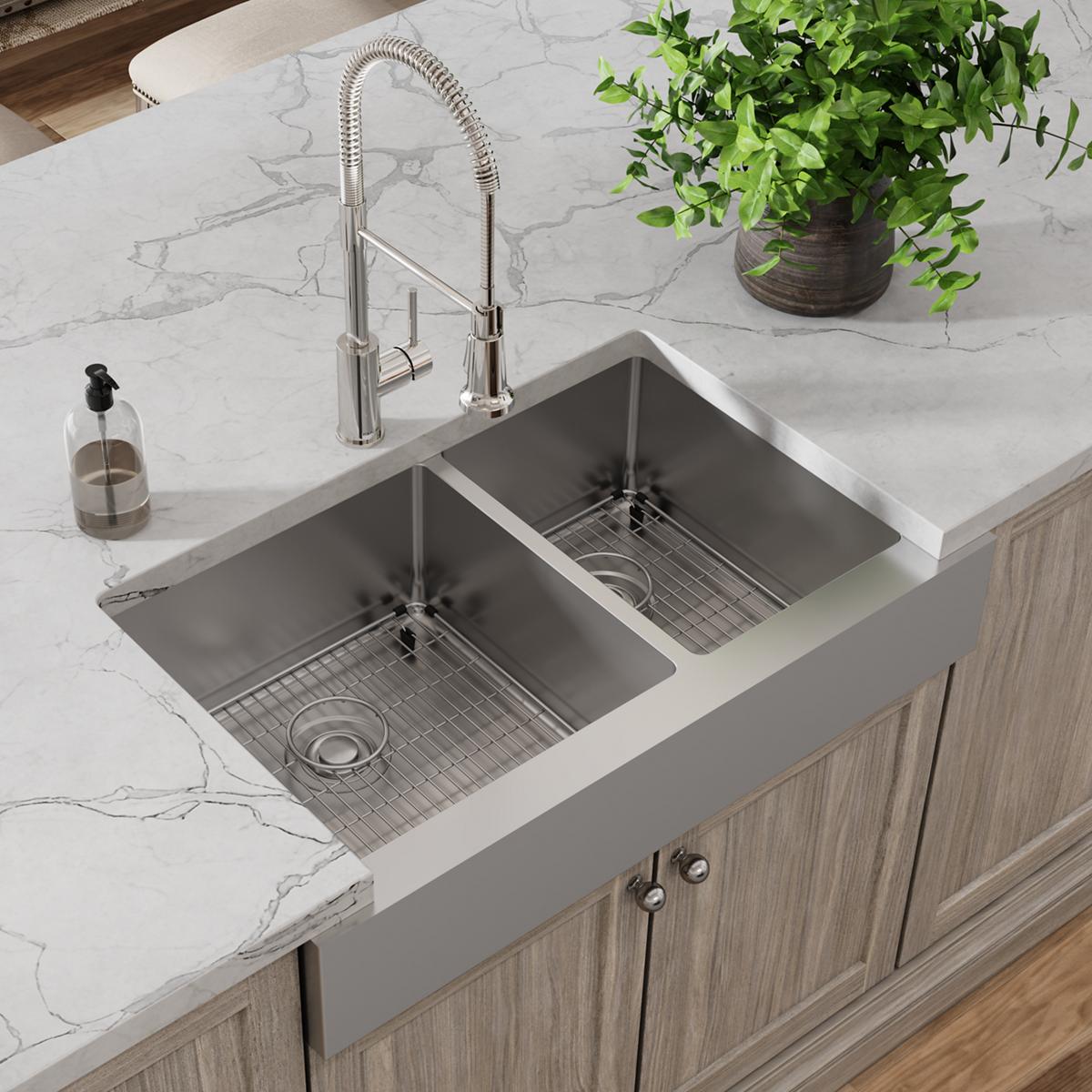 Stainless steel farmhouse sink with two unequal bowls, pull-down faucet, bottom grids, and drain strainer installed in white 