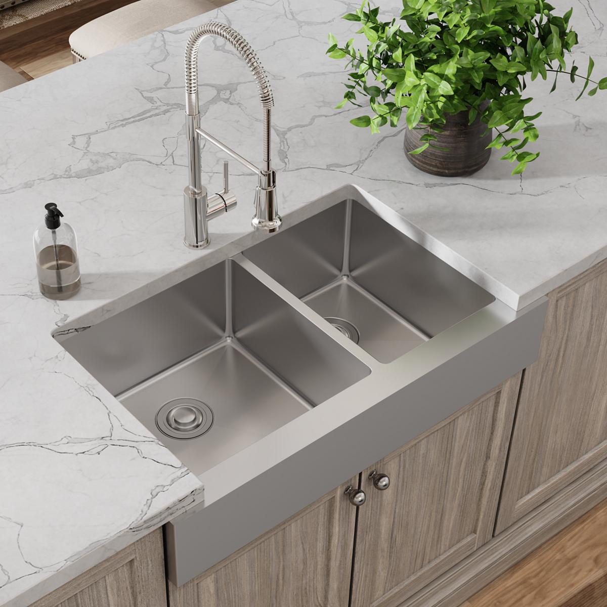 Stainless steel farmhouse sink with two unequal bowls and chrome pull-down faucet installed on marble countertop with wood ca