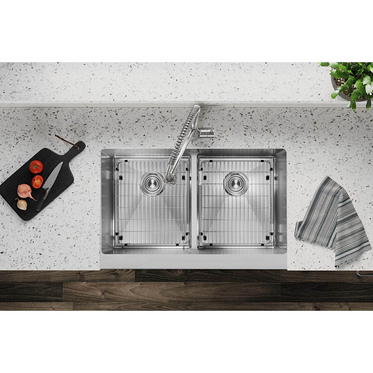 Stainless steel double bowl farmhouse sink with center divider, dual drains, and matching faucet installed in speckled counte