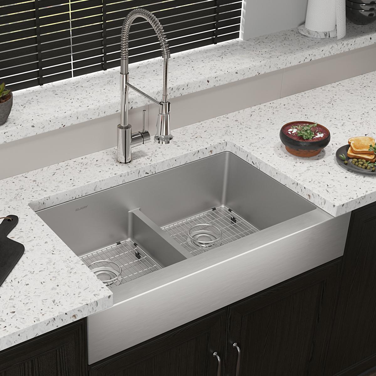 Stainless steel double bowl farmhouse sink with divider installed in quartz countertop, paired with pull-down spray faucet.