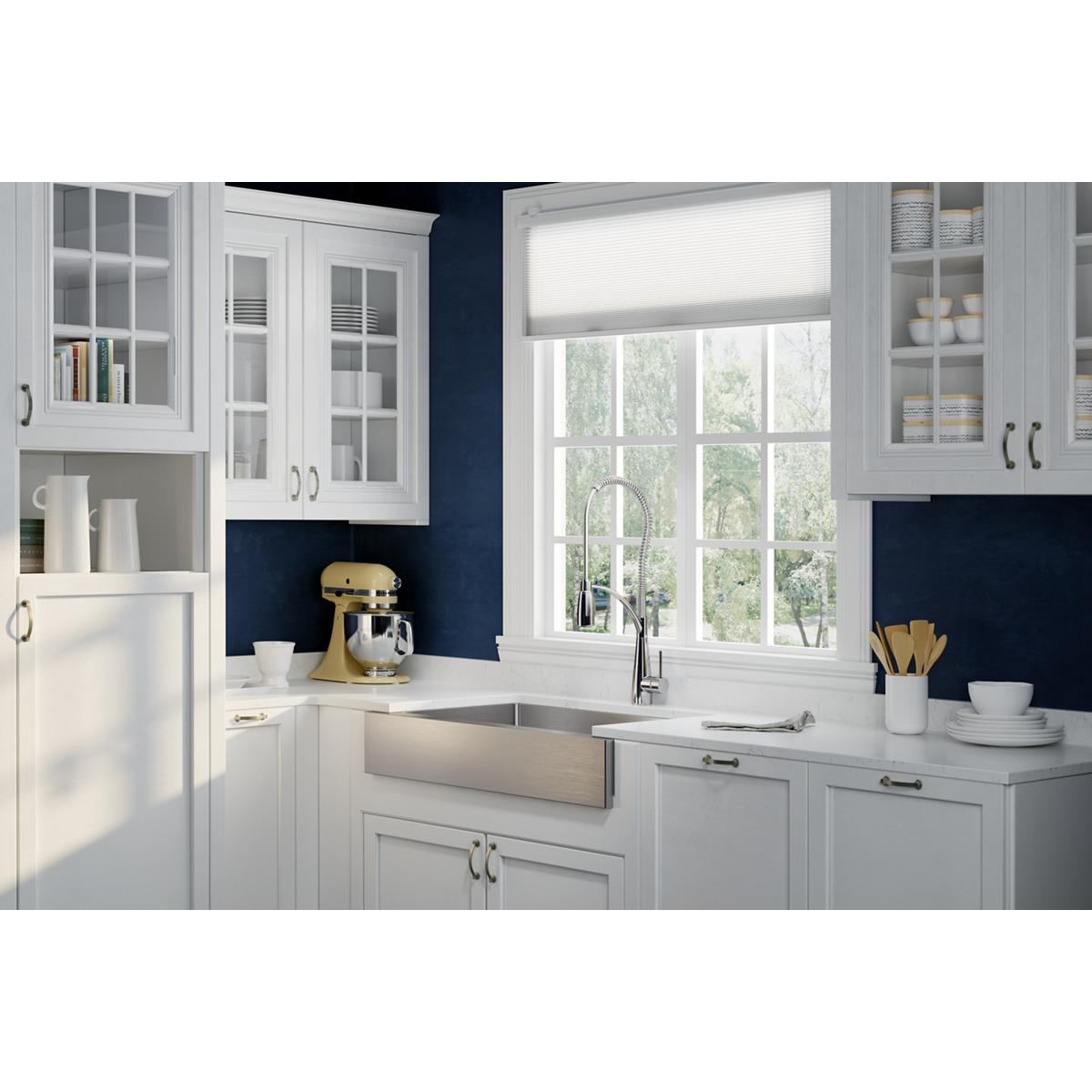 Stainless steel farmhouse sink with two equal bowls and center divider installed in white kitchen cabinetry below window.