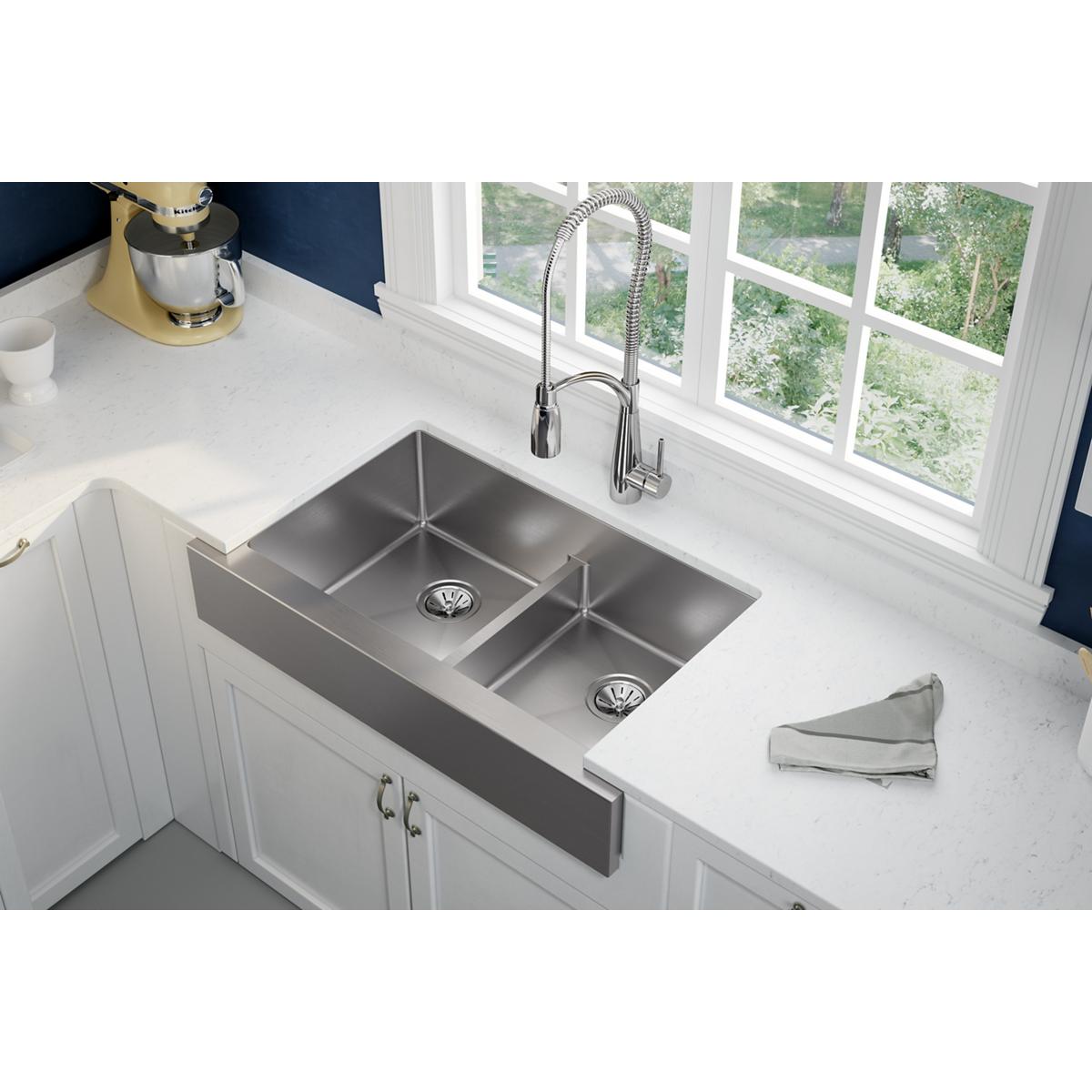 Stainless steel farmhouse sink with two equal bowls and divider, mounted in white countertop with spray faucet.